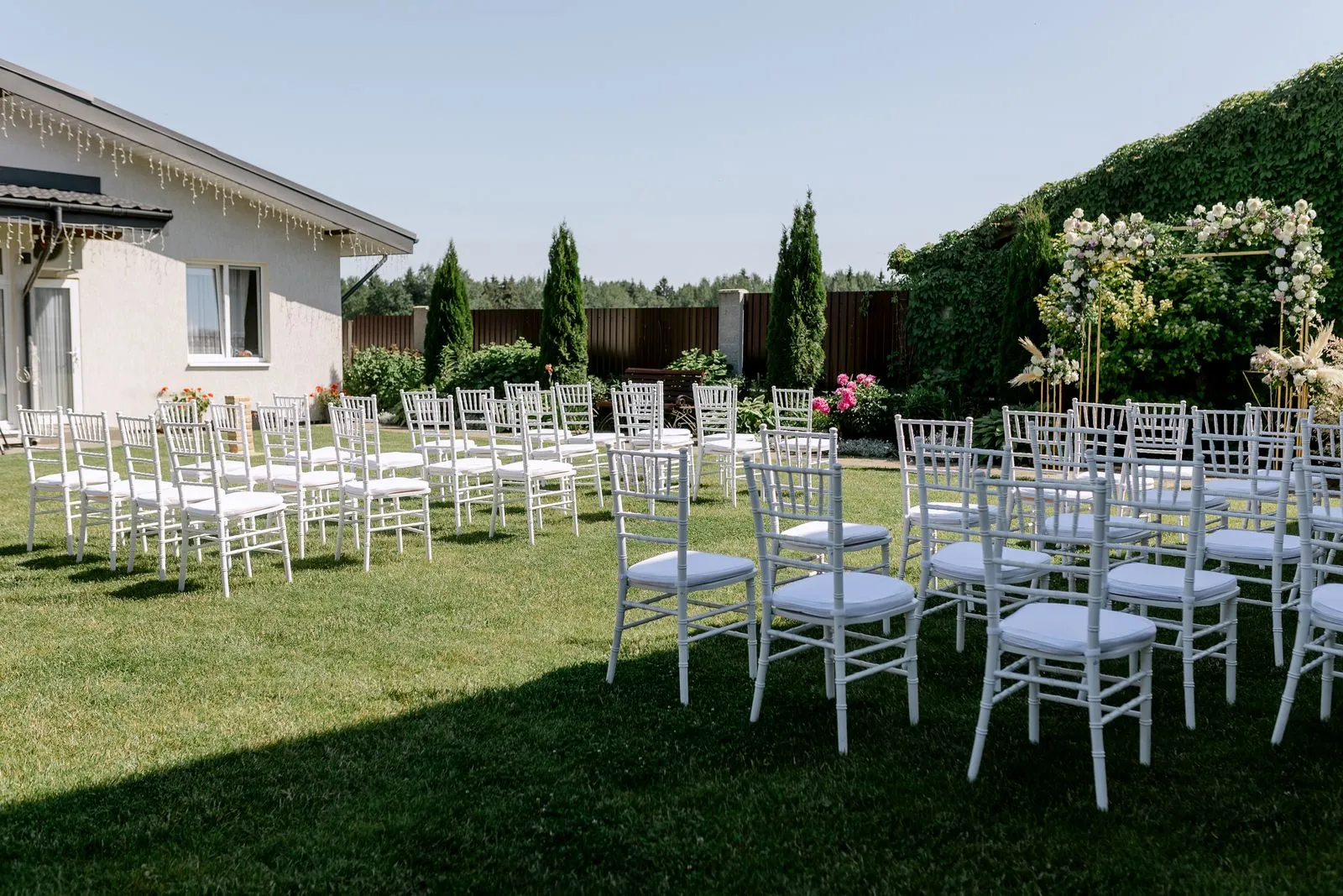 White chairs in a garden wedding ceremony setup on a green lawn — backyard wedding checklist